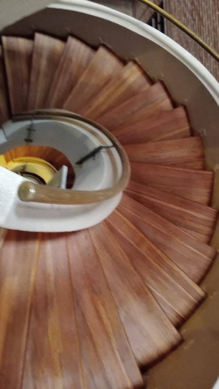 Detalle de peldaños en madera de escalera caracol con barandal dorado